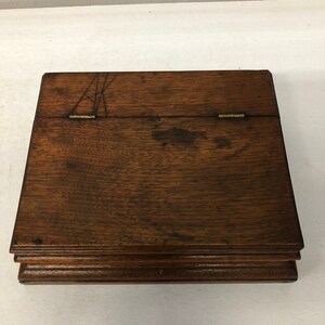May include: A wooden box with a hinged lid and a dark brown finish. The box has a simple design with a slightly raised edge around the top and bottom.