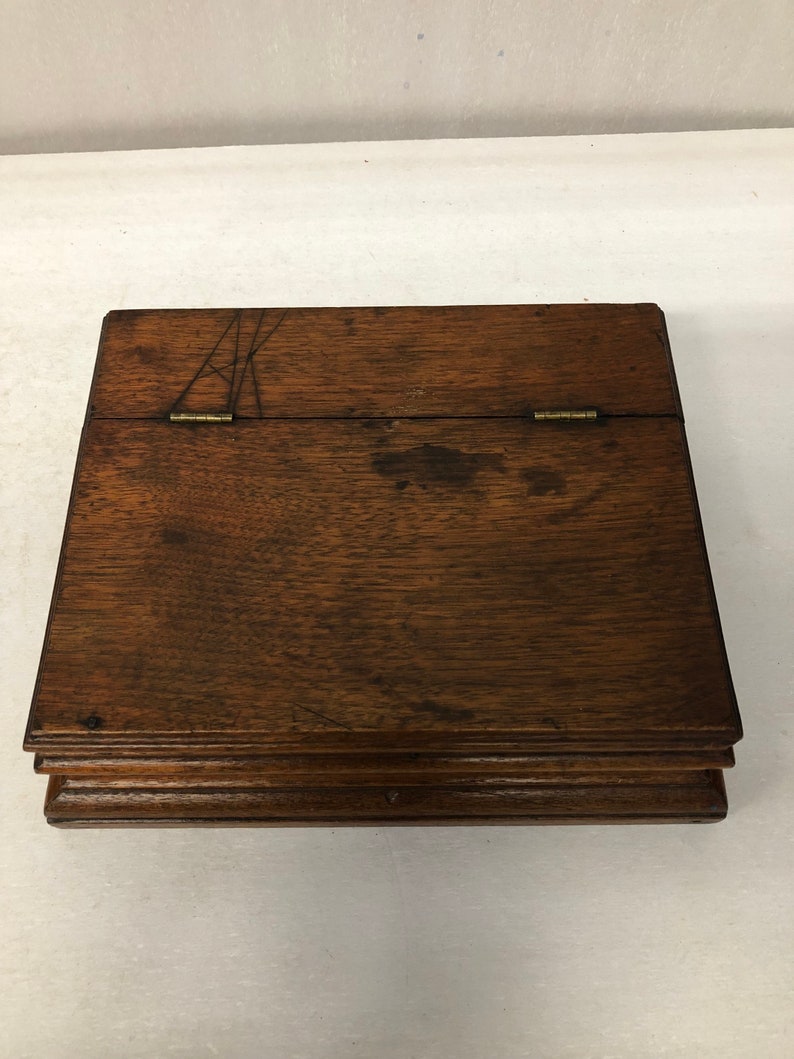 May include: A wooden box with a hinged lid and a dark brown finish. The box has a simple design with a slightly raised edge around the top and bottom.