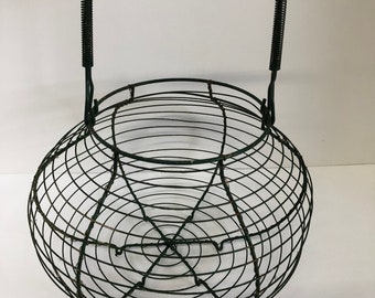 May include: A black wire basket with a spring handle. The basket is round and has a wire mesh design.