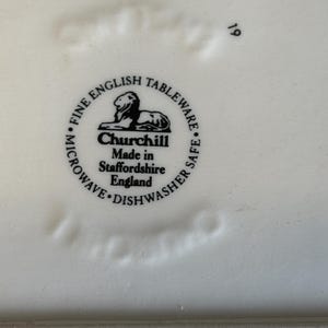 Peut inclure: Gros plan sur une assiette en c&eacute;ramique blanche avec le texte "FINE ENGLISH TABLEWARE" et "Churchill Made in Staffordshire England" dans un motif circulaire noir. L'assiette est adapt&eacute;e au micro-ondes et au lave-vaisselle.