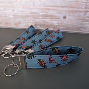 May include: A blue fabric key chain with a colorful bug pattern. The key chain has a silver metal ring and a silver metal clasp.
