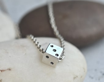 Könnte beinhalten: Eine silberne Kettenkette mit einem kleinen silbernen Würfel-Anhänger. Der Würfel hat schwarze Punkte auf jeder Seite.