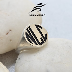 May include: A silver signet ring with a black oval inlay featuring the initials "NLC" in a bold, modern font.