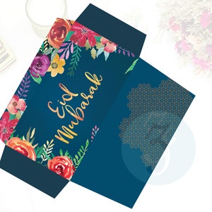 Puede incluir: Un sobre azul con un dise&ntilde;o floral y letras doradas que dicen "Eid Mubarak". El sobre tiene un patr&oacute;n geom&eacute;trico dorado en la parte posterior.
