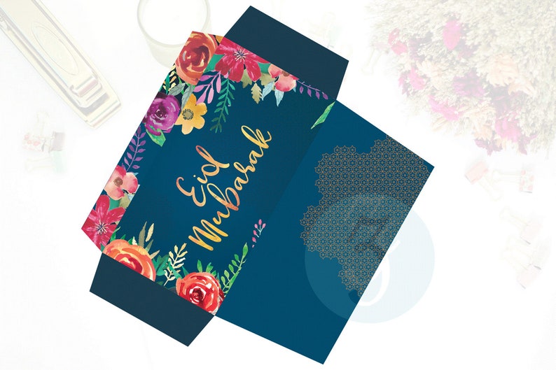 Puede incluir: Un sobre azul con un dise&ntilde;o floral y letras doradas que dicen "Eid Mubarak". El sobre tiene un patr&oacute;n geom&eacute;trico dorado en la parte posterior.