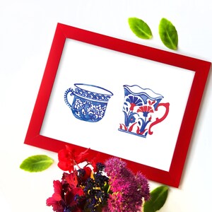 May include: A watercolor painting of two teacups. One teacup is blue and white with a floral design. The other teacup is red, blue, and white with a floral design. The teacups are framed in a red frame.