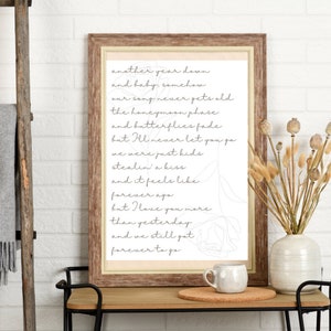 May include: A framed print with a white background and black text. The text reads "another year down and baby, somehow our song never gets old the honeymoon phase and butterflies fade but I'll never let you go we were just kids stealin' a kiss and it feels like forever ago but I love you more than yesterday and we still got forever to go".