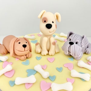 May include: A yellow cake decorated with three fondant dogs, white bone shapes, and pink and blue hearts.