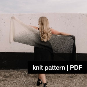 May include: A knitted shawl with a gradient effect, transitioning from white to grey and black. The text "knit pattern | PDF" is displayed on a black bar. The shawl is held up against a white wall.