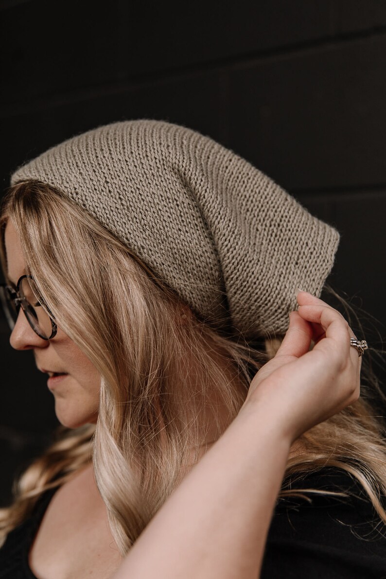 May include: A woman wearing a light brown knitted beanie hat. The hat is slouchy and has a simple design.
