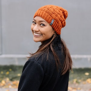 May include: An orange knitted beanie hat with a textured design and a small grey tag. The hat is made of a soft, warm material, ideal for cold weather. A stylish accessory for any wardrobe.