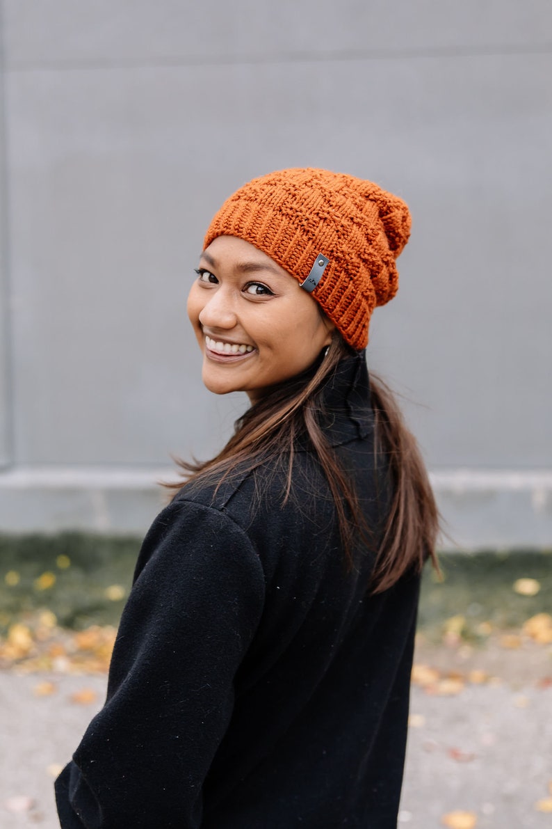 May include: An orange knitted beanie hat with a textured design and a small grey tag. The hat is made of a soft, warm material, ideal for cold weather. A stylish accessory for any wardrobe.