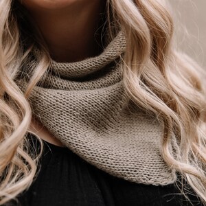 May include: A close-up of a woman wearing a brown knitted scarf. The scarf is folded in a triangular shape and is worn around the neck.
