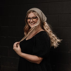 May include: A woman with long blonde hair wearing a grey beanie and black dress, smiling at the camera.