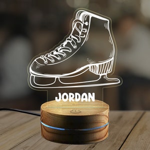 May include: A white outline of an ice skate with the name "JORDAN" printed below it. The skate is on a wooden base with a blue light ring around the base.