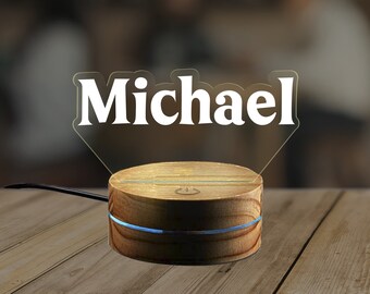 May include: A wooden base with a blue light ring and a power button on the top. The base is holding a clear acrylic plaque with the name "Michael" in white lettering.