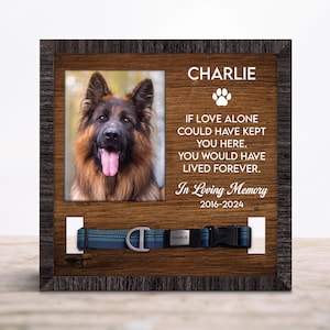 May include: A wooden pet memorial frame featuring a photo of a German Shepherd. The frame includes the name "Charlie", a paw print, and the text "If love alone could have kept you here, you would have lived forever. In Loving Memory 2016-2024". A dog collar is displayed.
