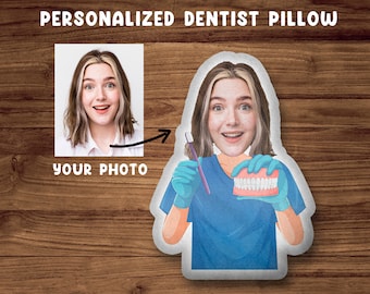 May include: A personalized pillow featuring a cartoon dentist holding a set of dentures and a dental tool. The dentist has a blue scrub top and is smiling. The pillow is white and has a space for a photo to be added.
