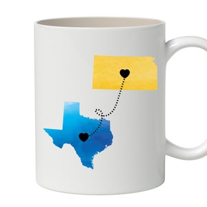 May include: White ceramic mug with a blue and yellow watercolor illustration of Texas and Kansas with black hearts and a dotted line connecting them.