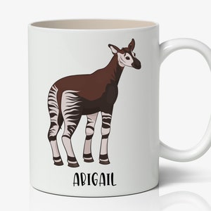 May include: White ceramic mug with a brown and white okapi illustration and the name "ABIGAIL" printed in black at the bottom.