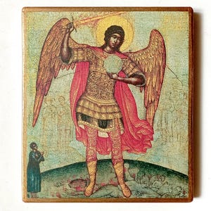 May include: A rectangular wooden icon featuring a painted depiction of an angel with large wings, wearing ornate gold armor and a flowing red cloak. The figure holds a sword raised overhead and a circular orb, standing above a small dark figure.