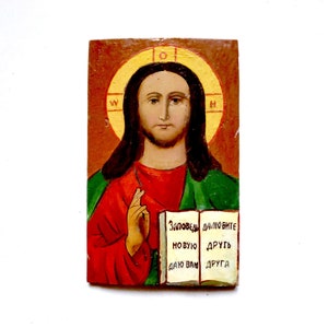 May include: A hand-painted icon of Jesus Christ with a halo and a red robe. The icon is on a wooden panel and includes the text "Заповеди далюбите новую друг даю вам друга".