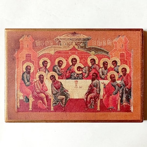 May include: A rectangular religious icon showing a scene with figures around a table. The artwork uses warm tones of red, gold, and brown. The figures have halos, and the icon is framed with a decorative border.