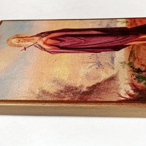 K&ouml;nnte beinhalten: Rechteckige Holzplakette mit religi&ouml;ser Malerei. Das Kunstwerk zeigt eine Figur in einem langen, weinroten Gewand, die ein Kreuz h&auml;lt. Der Hintergrund hat eine Landschaft mit warmen Erdt&ouml;nen und einem goldenen Rahmen.
