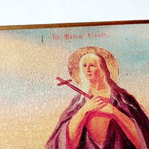 K&ouml;nnte beinhalten: Vintage religi&ouml;se Illustration einer Frau mit Heiligenschein und Kreuz. Das Bild hat ein gealtertes Aussehen mit sichtbaren Rissen. Der Text "The Maria Gruner" ist oben sichtbar. Vintage-&Auml;sthetik.