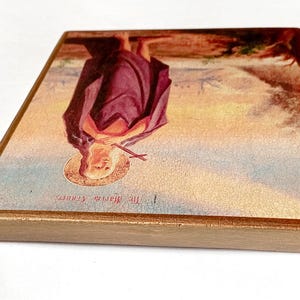 K&ouml;nnte beinhalten: Ein religi&ouml;ses Holzikon mit einer Figur in einem lila Gewand mit Heiligenschein, die ein Kreuz h&auml;lt. Das Bild hat einen goldenen Rand und ist vor einem Landschaftshintergrund platziert. Der Text "The Maria Shrine" ist sichtbar.