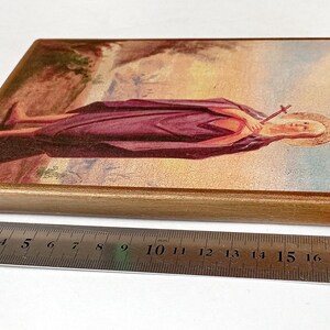 K&ouml;nnte beinhalten: Rechteckige religi&ouml;se Holz-Ikone mit einer Figur in einem lila Gewand, die ein Kreuz h&auml;lt. Die Ikone hat einen goldenen Rand und ist etwa 20 cm lang. Das Bild ist vor einem Landschaftshintergrund.
