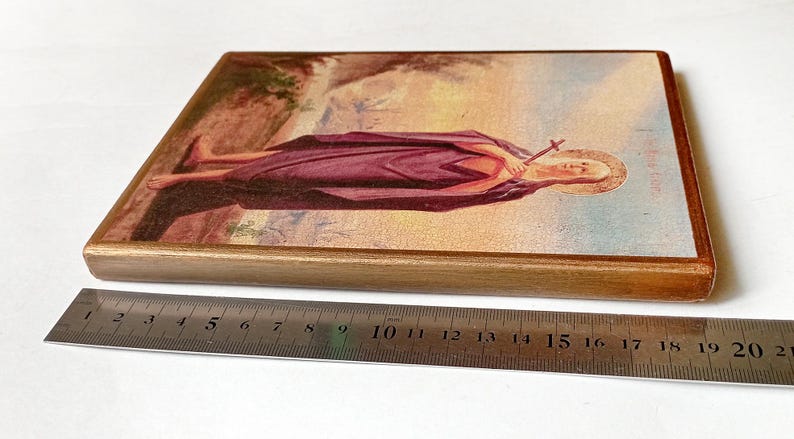 K&ouml;nnte beinhalten: Rechteckige religi&ouml;se Holz-Ikone mit einer Figur in einem lila Gewand, die ein Kreuz h&auml;lt. Die Ikone hat einen goldenen Rand und ist etwa 20 cm lang. Das Bild ist vor einem Landschaftshintergrund.