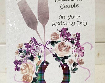 Peut inclure: Une carte de mariage avec un fond blanc et un motif floral. La carte représente deux flûtes de champagne avec un fer à cheval attaché à un ruban. Le fer à cheval est décoré d'un motif écossais. Le texte sur la carte dit "To A Beautiful Couple On Your Wedding Day".