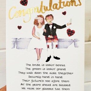 Puede incluir: Una tarjeta de boda con una ilustraci&oacute;n de dibujos animados de una novia y un novio con atuendos tradicionales escoceses. La tarjeta tiene una inscripci&oacute;n en pan de oro que dice "Felicidades". El texto en la tarjeta dice: "The bride is lookin' bonnie, The groom is lookin' grand, They walk doon the aisle thegither, Securely hand in hand, Their future's noo afore them, An' the years ahead are blessed, We raise oor glasses tae them, An' wish them a' the best, Tae the bride and groom!"