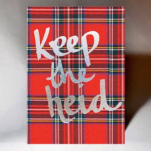 以下が含まれることがあります： 赤と黒の格子柄のカードに、銀色のグリッター文字で「Keep the heid」と書かれています。