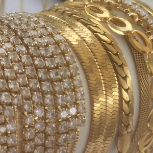 May include: A stack of gold bracelets with different designs, including a diamond-encrusted bracelet, a snake chain bracelet, and a chain link bracelet.