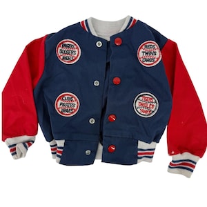 May include: A vintage baseball-style jacket in navy blue with red sleeves. The jacket features patches with team names like Dodgers, Angels, Reds, Twins, Cubs, Pirates, Orioles, and Yankees. It has a gray collar and cuffs with red and white stripes.
