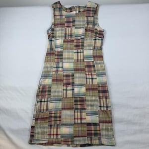 May include: Sleeveless patchwork dress featuring a variety of plaid patterns in shades of beige, red, green, and blue. The dress has a straight, knee-length cut and a round neckline. The fabric appears to be a lightweight cotton or linen blend.