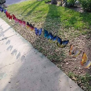 May include: A line of colorful butterfly garden decorations in various shades of blue, red, yellow, and purple. The butterflies are arranged in a row on a grassy lawn.