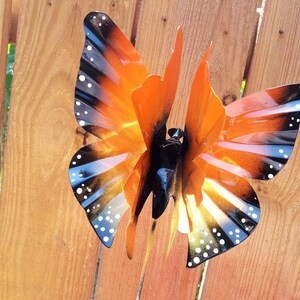 May include: A metal butterfly wind spinner with orange, black, and white paint. The butterfly has a detailed design with black and white spots on the wings.