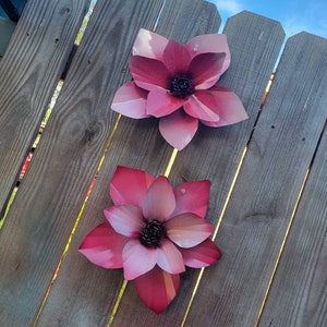 Puede incluir: Dos flores de metal rosa con un acabado texturizado est&aacute;n unidas a una valla de madera. Las flores tienen un dise&ntilde;o 3D y son de color rosa claro con un centro rosa m&aacute;s oscuro.