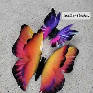 May include: Three metal butterflies in a gradient of pink, orange, and purple. The butterflies are in different sizes, with the largest measuring 12-13 inches and the smallest measuring 8-9 inches.  "Small 8-9 inches" and "Large 12-13 inch" are written in white text on a black background.