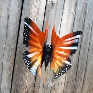 May include: Orange and black metal butterfly garden stake with white polka dots. The butterfly is in a flying position with its wings spread out.