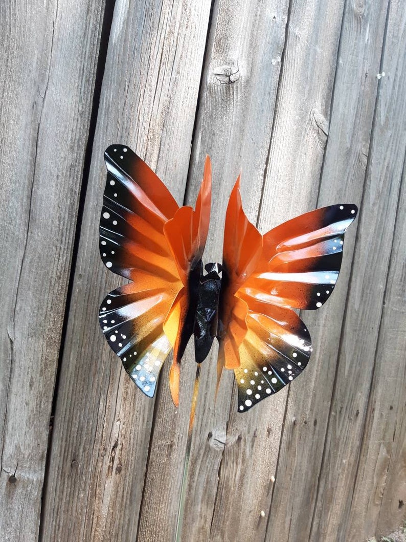 May include: Orange and black metal butterfly garden stake with white polka dots. The butterfly is in a flying position with its wings spread out.