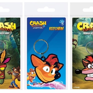 May include: Three Crash Bandicoot rubber keychains. The first keychain features a mask with feathers. The second keychain features Crash Bandicoot's face. The third keychain features Crash Bandicoot's face with a toothy grin.