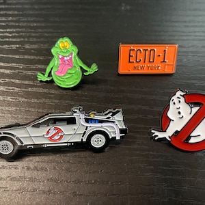 May include: Four enamel pins featuring characters and vehicles from the Ghostbusters and Back to the Future franchises. The pins include a green ghost, a red no ghost sign, a grey DeLorean time machine, and an orange license plate that reads "ECTO-1 NEW YORK".