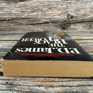 May include: A hardcover book titled "The Black Tower" by P.D. James. The book has a black cover with white lettering and a picture of a person. The book's pages are aged, and the spine is slightly worn.