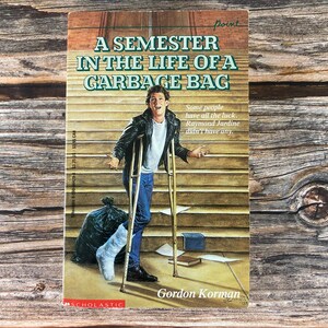 May include: A book cover with a young man on crutches, a black garbage bag, and the title "A Semester in the Life of a Garbage Bag" by Gordon Korman. The book is part of the Point series.