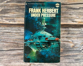May include: A vintage paperback book cover featuring a blue and white spaceship in the ocean. The book title is "Frank Herbert Under Pressure" and the subtitle is "(Originally: The Dragon in the Sea)".