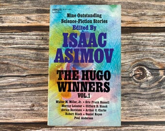 May include: A vintage paperback book cover with a colorful abstract background. The title is "The Hugo Winners, Vol. 1" and the book is edited by Isaac Asimov. The cover features the names of the authors of the nine science fiction stories included in the book.